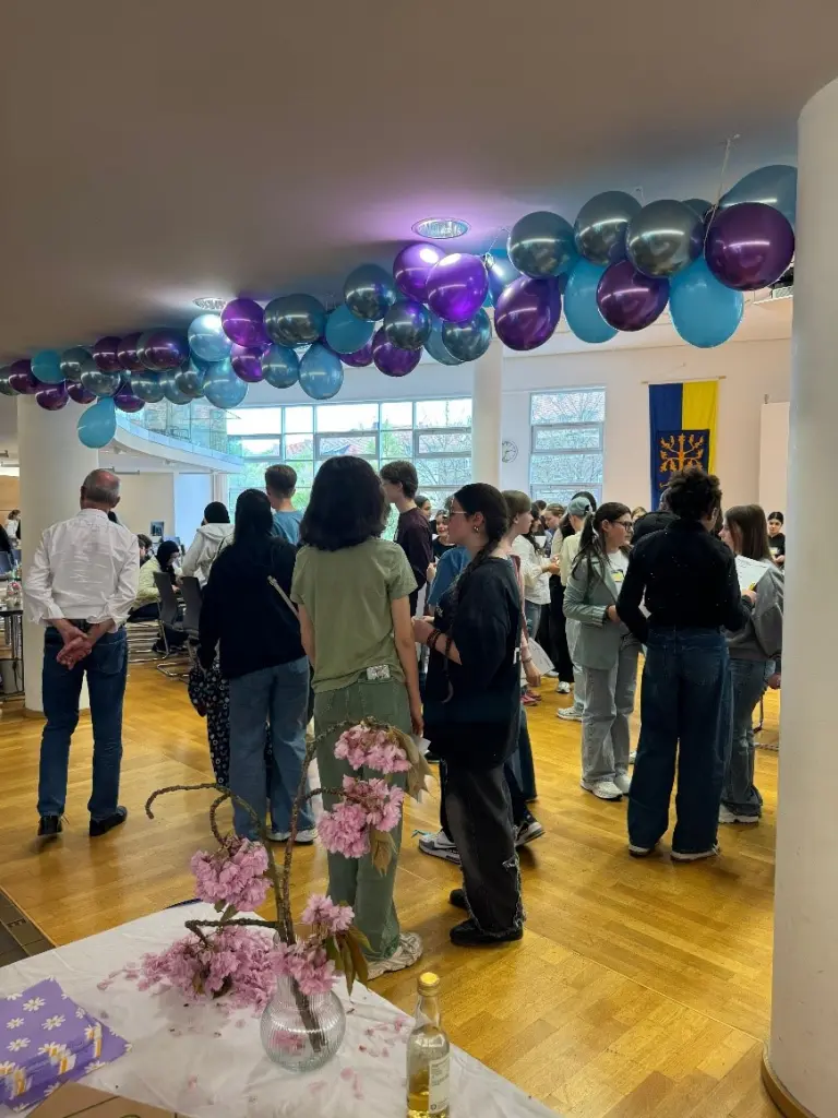 Foto: Im Ratssaal haben sich viele Jugendliche versammelt, die in kleineren Gruppen zusammenstehen und miteinander sprechen. Die Decke ist mit bunten Luftballons dekoriert.