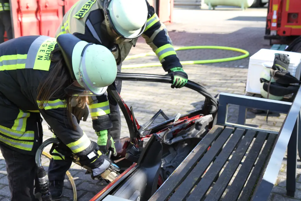 Foto: Zwei Personen in Feuerwehruniform schneiden mit einem Metallschneidegerät eine Autotür auf.