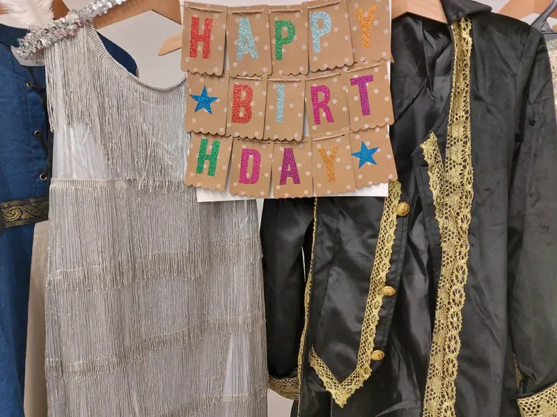 Foto: Ein Schild mit der Aufschrift "Happy Birthday" hängt neben historischen Kleidungsstücken auf einer Stange.