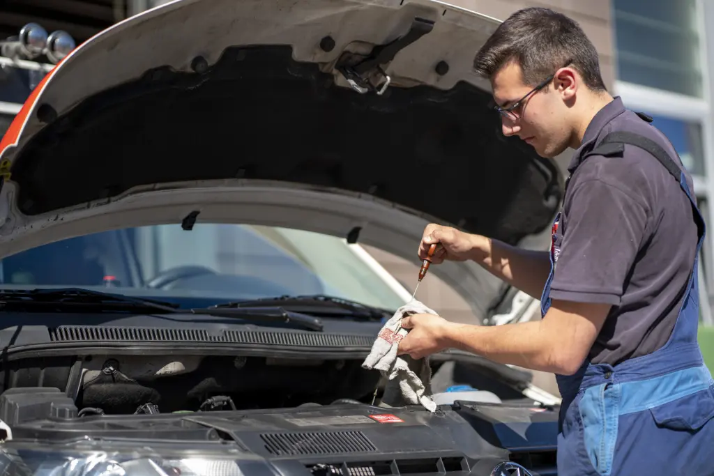 Ein Kraftfahrzeugmechatroniker pr&uuml;ft im Seitenprofil den &Ouml;lstand an einem Notarzteinsatzfahrzeug. Die Szene zeigt die sorgf&auml;ltige Wartung und Instandhaltung von Einsatzfahrzeugen bei der Feuerwehr.st.