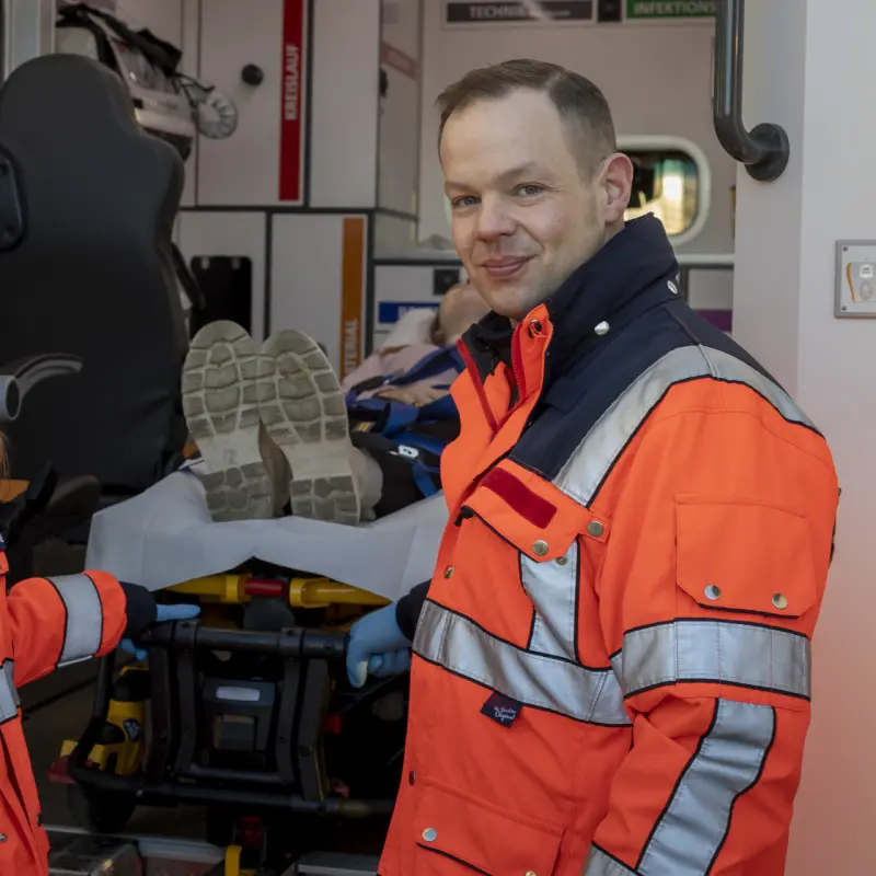 Foto: EIne Notfallsanit&auml;terin und ein Notfallsanit&auml;ter stehen an der offenen Klappe eines Rettungswagens, in dem eine Person liegt.