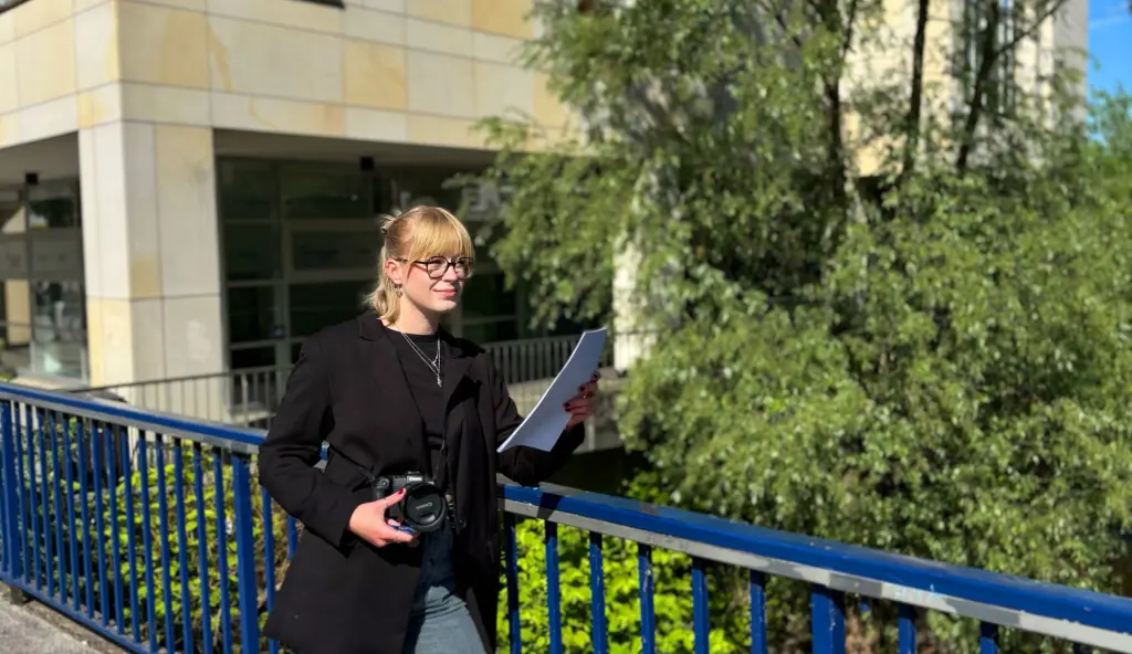 Eine weibliche Volont&auml;rin in der Pressestelle h&auml;lt einen Stift, einen Notizblock und eine Kamera in der Hand. Die Aufnahme zeigt die vielseitige und engagierte Arbeit im Bereich Presse- und &Ouml;ffentlichkeitsarbeit.