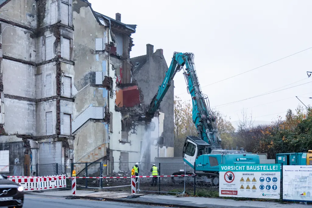 Ein Bagger reißt ein Haus ab und hebt mit seiner Schaufel Schutt hoch.