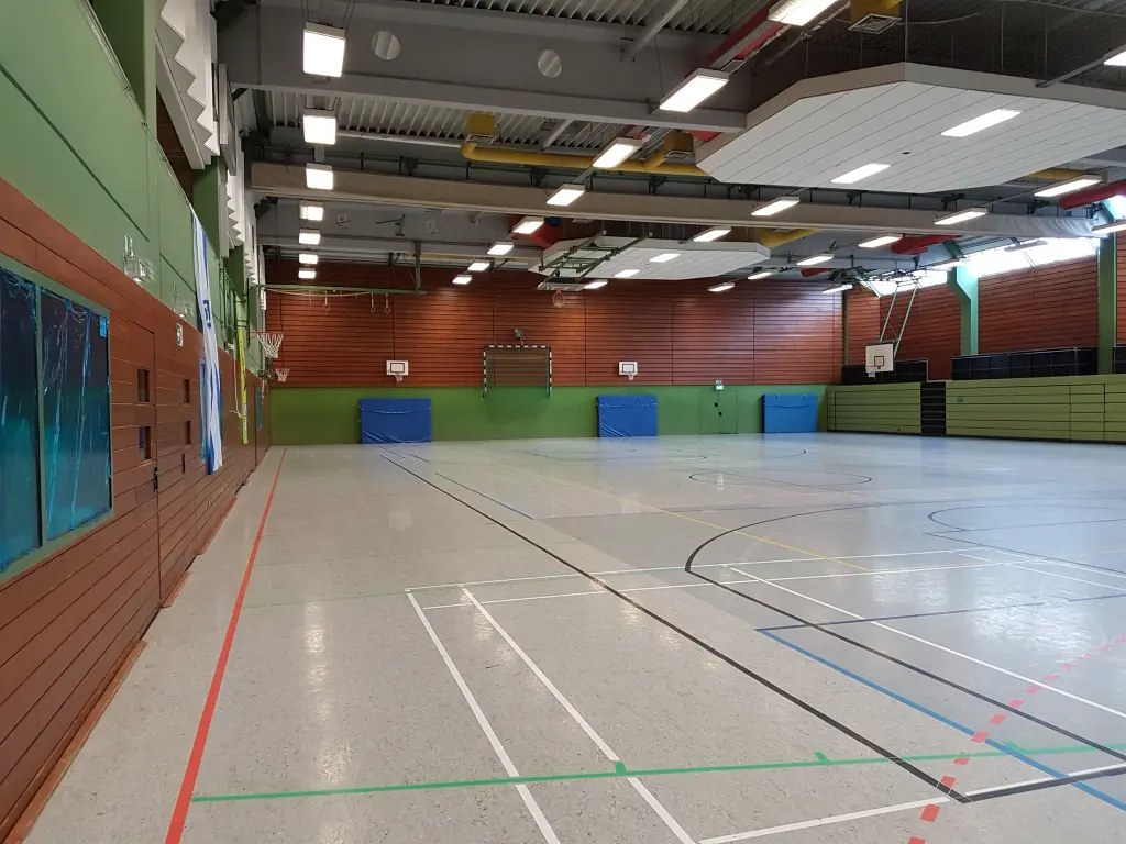 Foto: Eine Sporthalle mit verschiedenen Markierungen auf dem Hallenboden und großen Sportmatten an den Seiten.