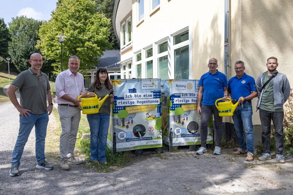 Foto: Eine Gruppe von Menschen steht mit Gießkannen in den Händen in einem Park.