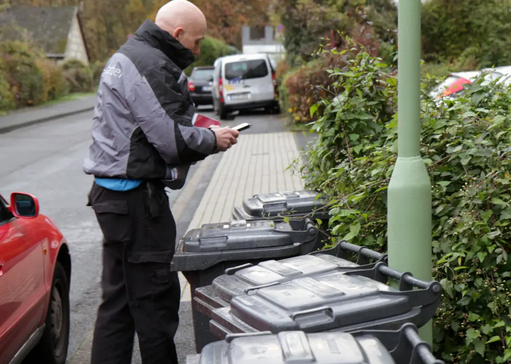 Foto: Ein Mitarbeiter der Müllentsorgung überprüft die korrekte Entsorgung von drei Mülltonnen auf einer Anwohnerstraße.