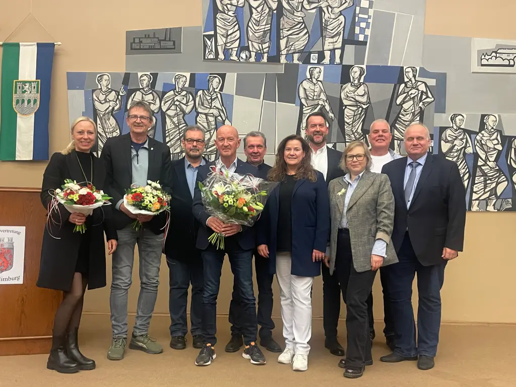 Foto: Eine Gruppe aus drei Frauen und sieben Männern stehen nahe beieinander. Einige von den Personen halten einen Blumenstrauß in der Hand.