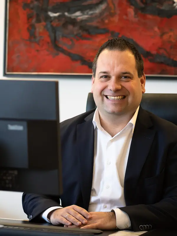 Foto: Dennis Rehbein sitzt an seinem Schreibtisch (ein Computerbildschirm sowie ein rotes Foto an der Wand sind zu sehen).
