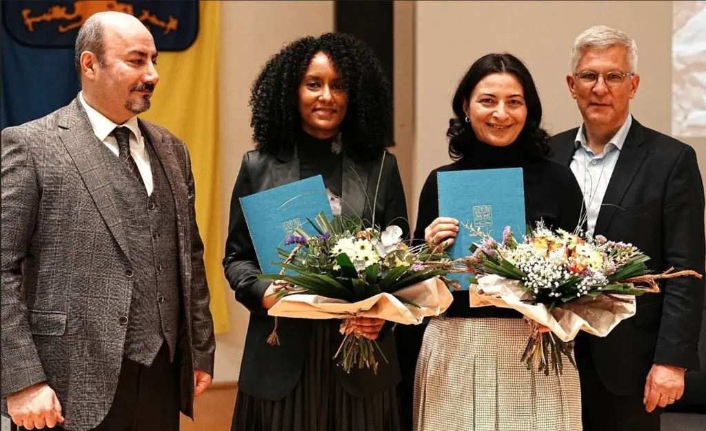 Foto: Zwei Frauen mit Urkunden und Blumensträußen stehen neben zwei Männern.