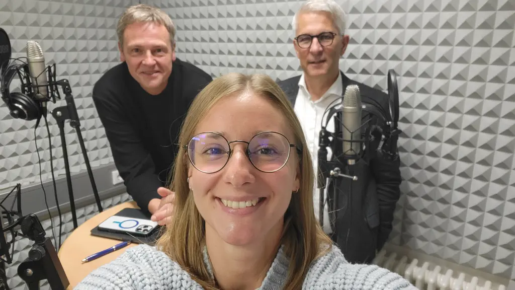 Foto: Drei Personen in einem Aufnahmestudio mit Mikros.