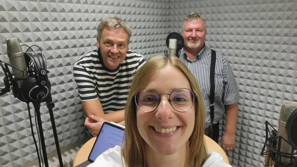 Foto: Drei Personen stehen in einem Studio vor Mikros.