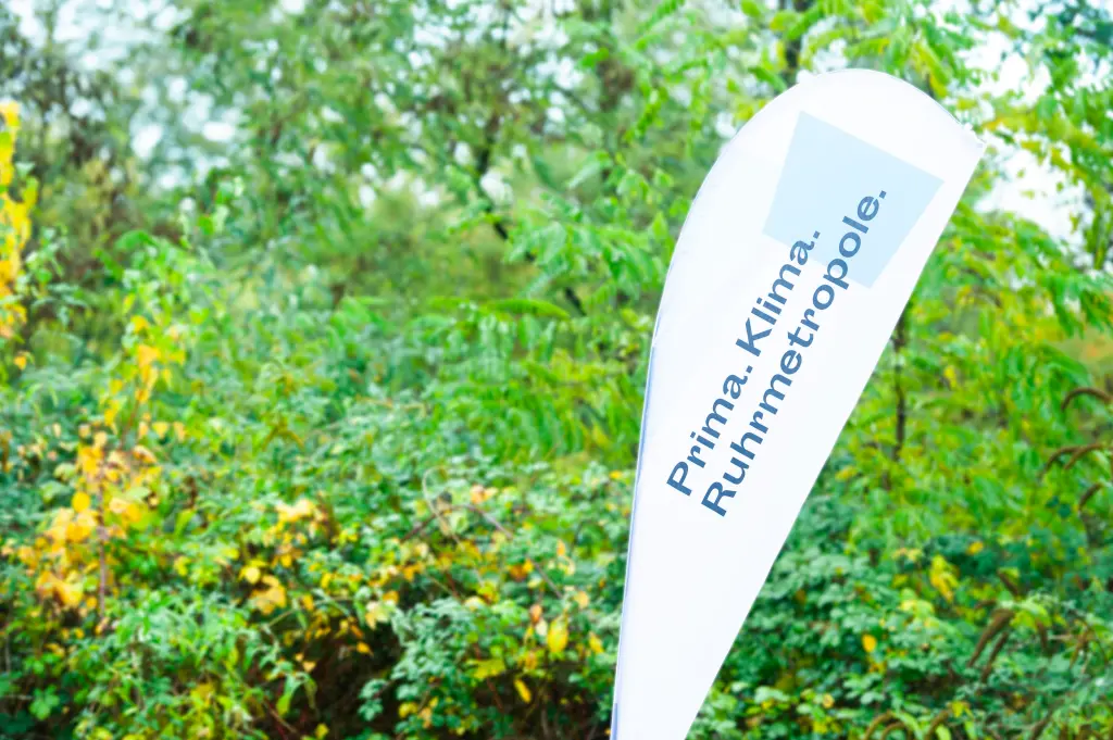 Foto: Eine Fahne mit der Aufschrift "Prima Klima Ruhrmetropole" vor einer grünen Hecke.