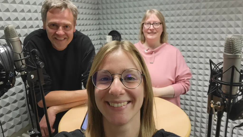 Drei Personen in einem Tonstudio. Zu sehen ist auch Aufnahmeequipment.