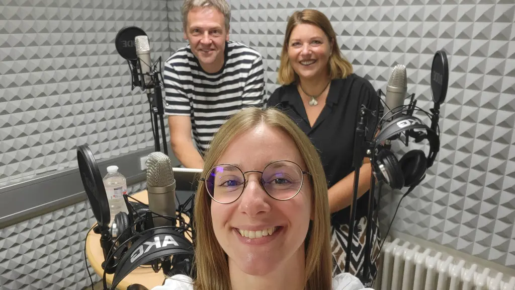 Foto: Drei Personen stehen in einem Studio vor Mikros.