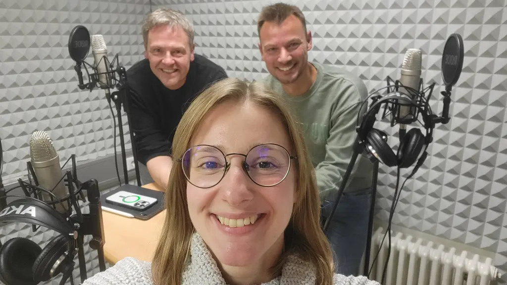 Drei Personen in einem Tonstudio, zu sehen sind auch Mikros und Kopfhörer.