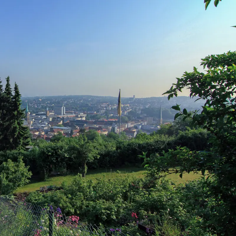 Foto: Im Vordergrund sind Bäume und ein Kleingarten zu sehen, in der Ferne die Dächer der Stadt Hagen.