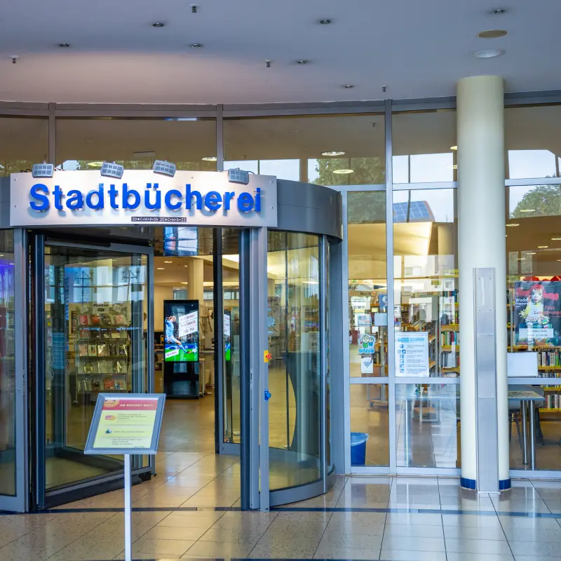 Foto: Der gläserne Eingang der Stadtbücherei mit automatischer Drehtür.