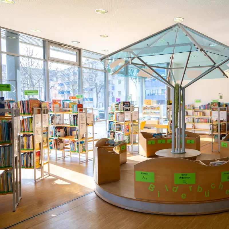 Foto: Zu sehen ist die Kinderbücherei in der Stadtbücherei auf der Springe mit einem Rondell und mehreren Bücherregalen.