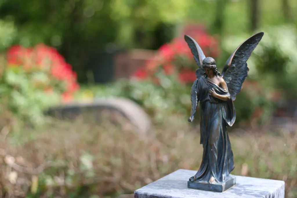 Foto: Nahaufnahme einer kleinen bronzenen Engelsfigur auf einem Grabstein.