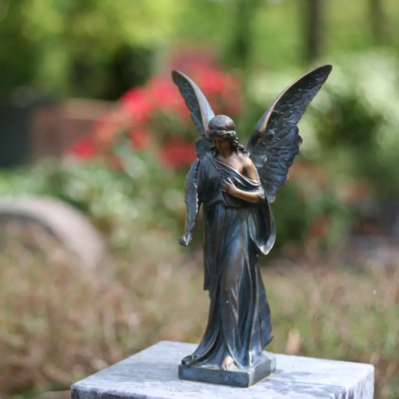 Foto: Nahaufnahme einer kleinen bronzenen Engelsfigur auf einem Grabstein.