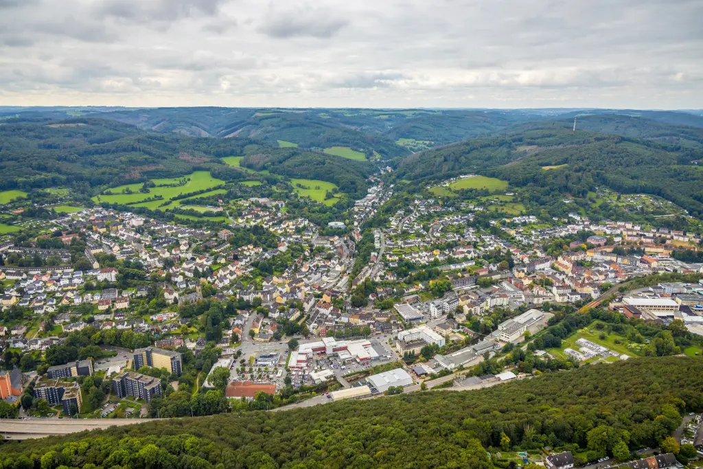 Foto: Das Luftbild eines Stadtteils, der zwsichen grünen Anhöhen liegt.