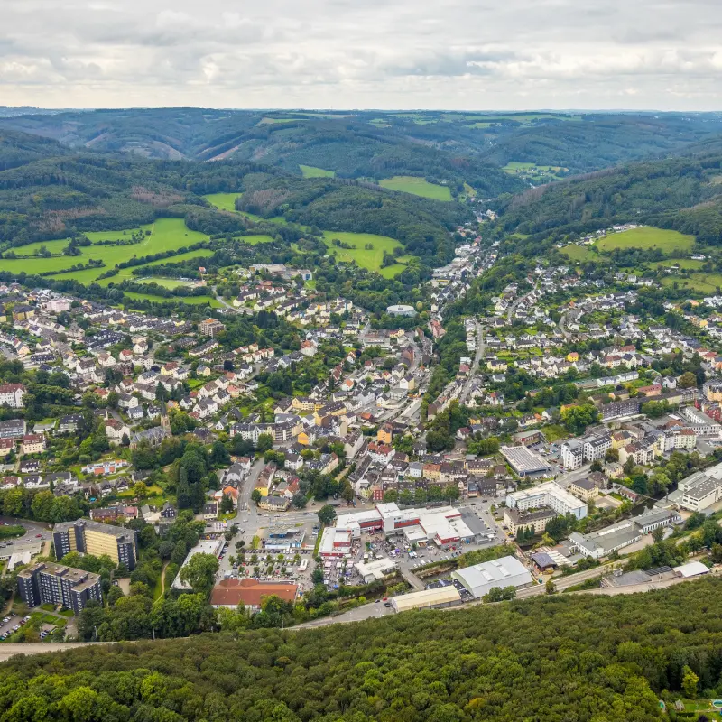 Foto: Das Luftbild eines Stadtteils, der zwsichen grünen Anhöhen liegt.