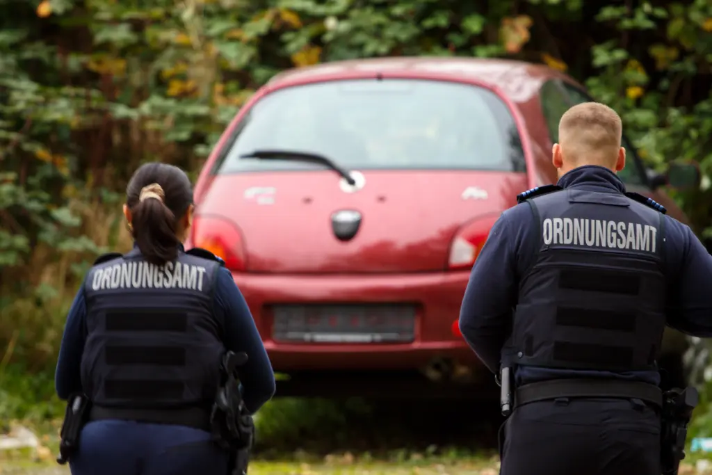 Foto: Zwei Mitarbeitende des Ordnungsamtes stehen vor einem Auto ohne Nummernschild.