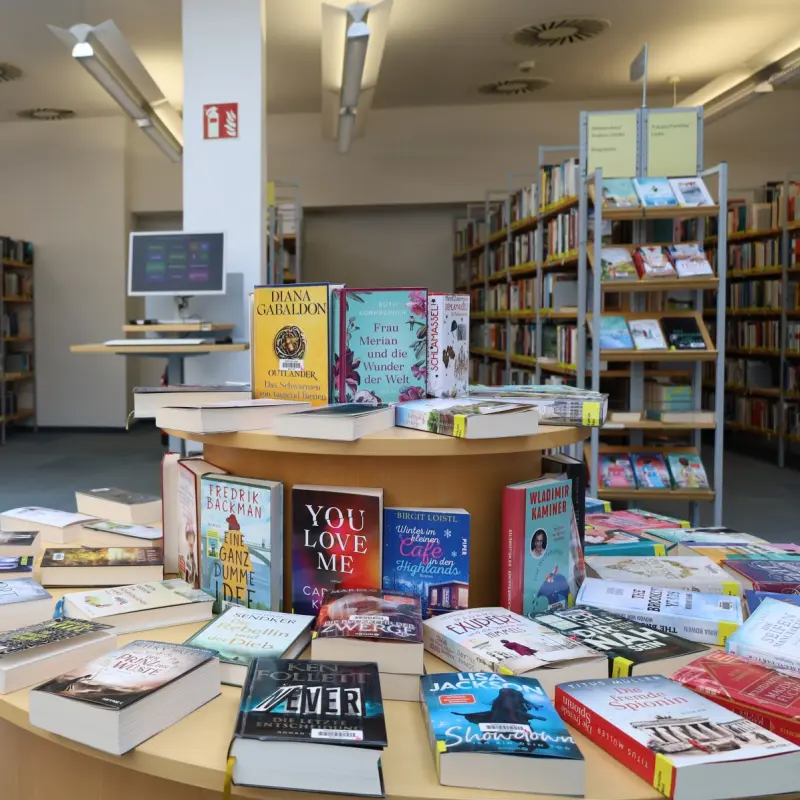 Eine Innenaufnahme einer B&uuml;cherei, im Vordergrund ein B&uuml;chertisch.