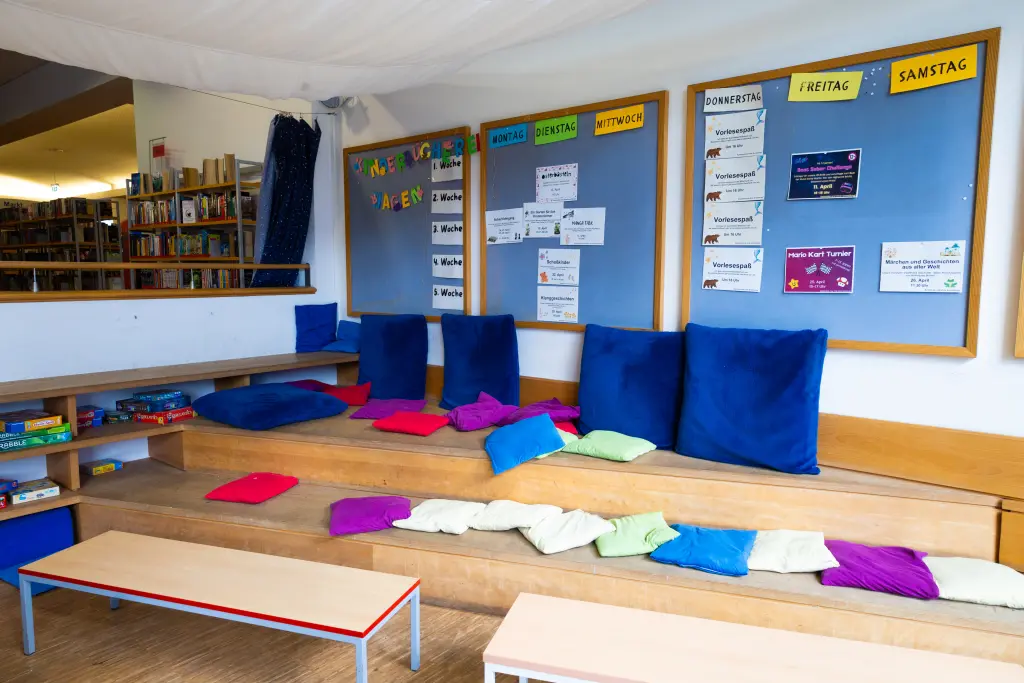 Foto: Zu sehen ist eine Leseecke für Kinder mit bunten Kissen und einer blauen Tafel im Hintergrund.