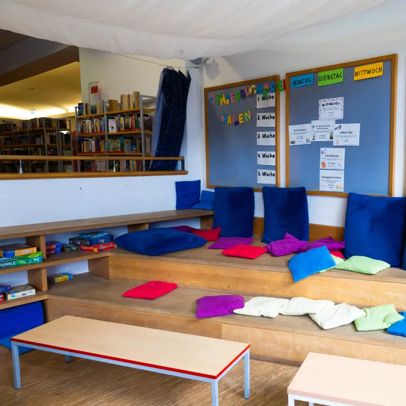 Foto: Zu sehen ist eine Leseecke für Kinder mit bunten Kissen und einer blauen Tafel im Hintergrund.