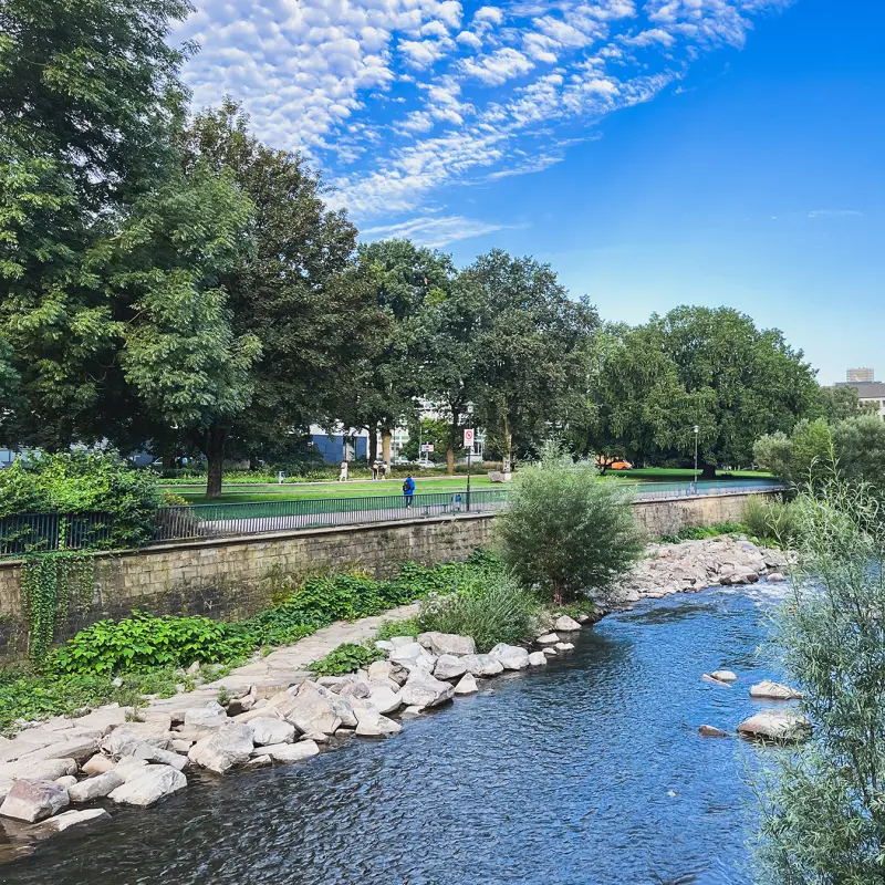 Foto: Grünflächen umgeben unter blauem Himmel die Volme.