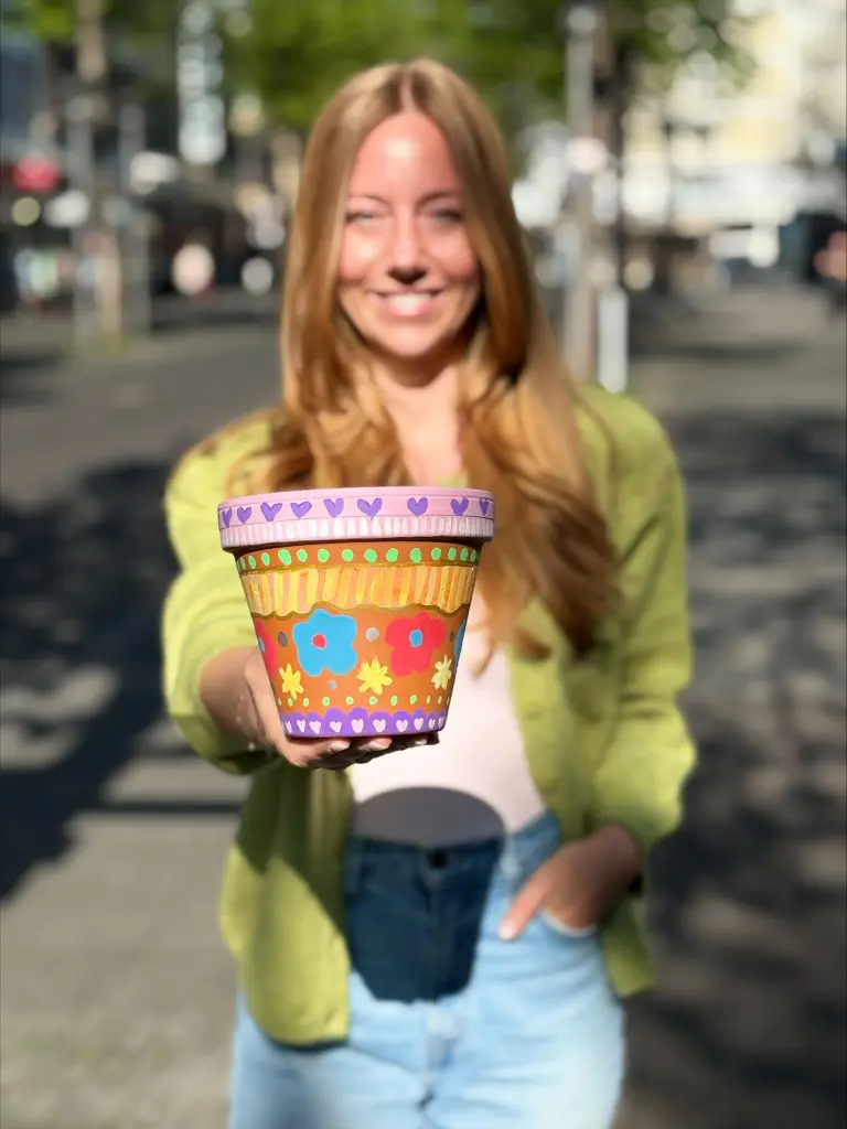 Foto: Eine Person h&auml;lt einen bunt bemalten Blumentopf in die Kamera.