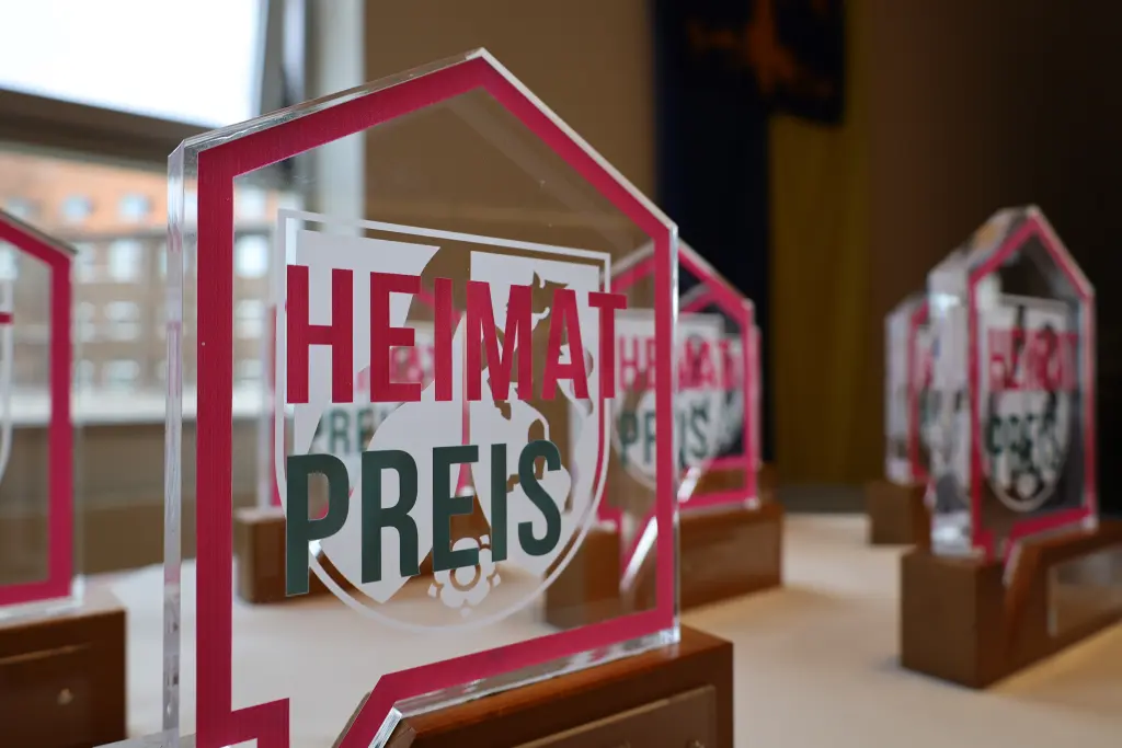 Foto: Bild einer Troph&auml;e (Eine Glasscheibe mit der Aufschrift "Heimatpreis"ist auf einem Holzpodest befestigt.