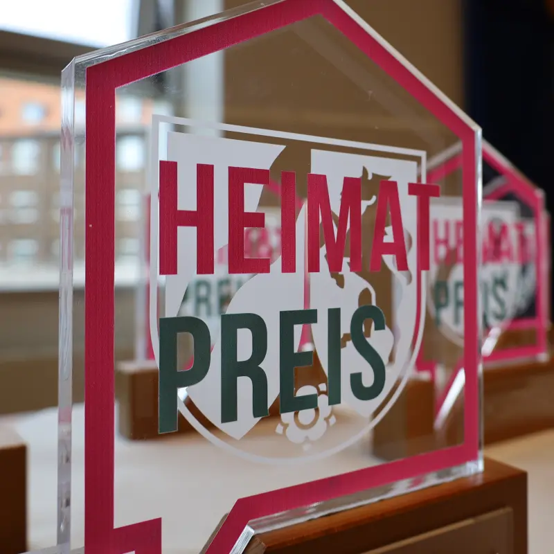 Foto: Bild einer Troph&auml;e (Eine Glasscheibe mit der Aufschrift "Heimatpreis"ist auf einem Holzpodest befestigt.