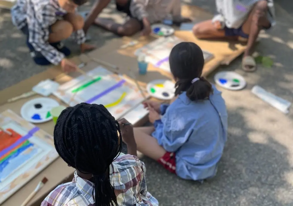 Foto: Vier Kinder sitzen an einer Holzplatte und malen Bilder mit bunten Farben.