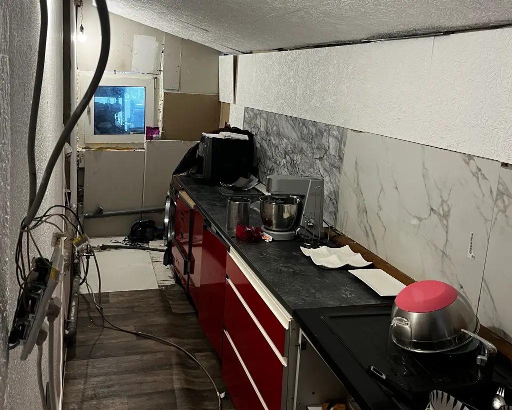 Foto: Eine verwahrloste K&uuml;che in einer Art Verschlag, mit notd&uuml;rftig verbauten Platten an den W&auml;nden und der Decke.