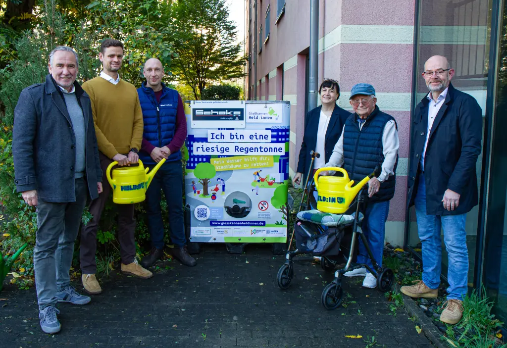 Foto: Eine Gruppe Männer und Frauen stehen in einem Garten vor einem großen Wassertank.