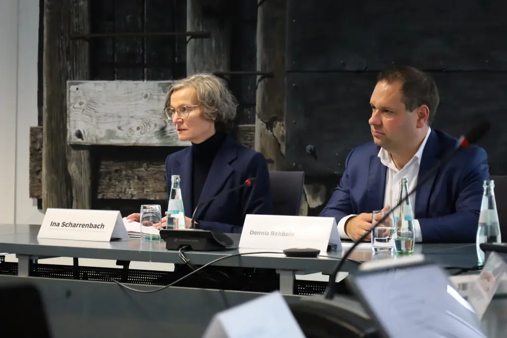 Foto: Ina Scharrenbach und Dennis Rehbei sitzen nebeneinander in einer Pressekonferenz, Frau Scharrenbach spricht in ein Mikrofon.