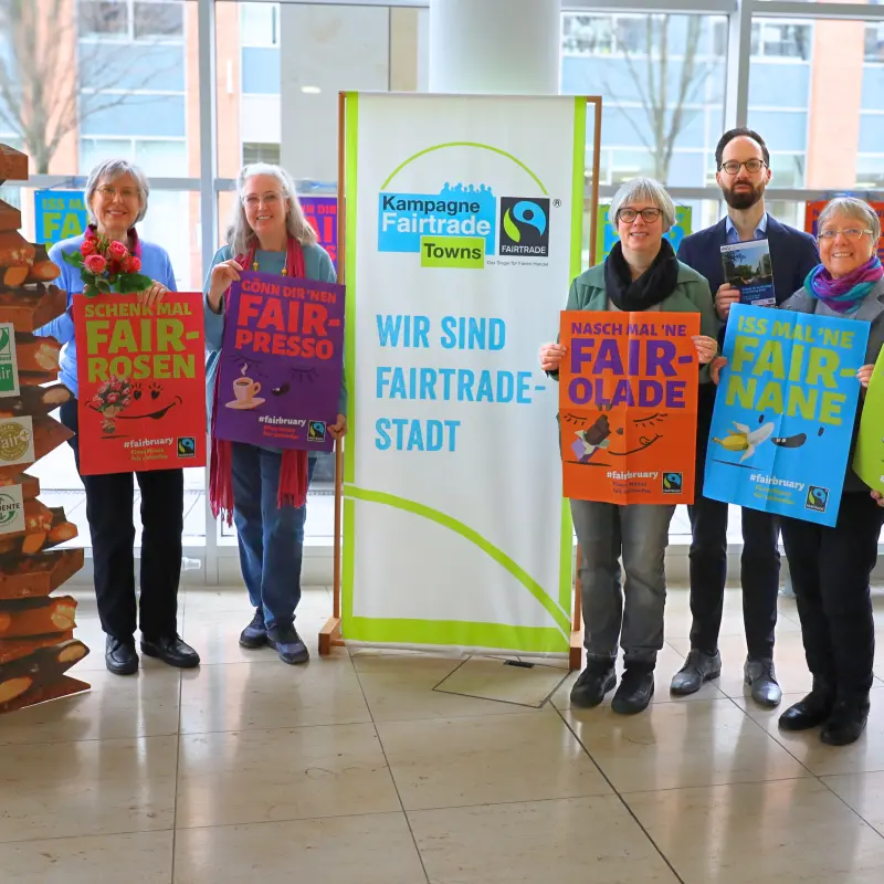 Gruppenbild: Beteiligte der Steuerungsgruppe Fair Trade Town Hagen mit bunten Plakaten und einem Banner zum Fairbruary.