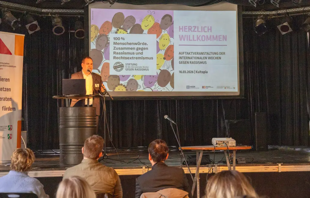 Foto: Ein Mann steht vor Publikum auf einer B&uuml;hne.