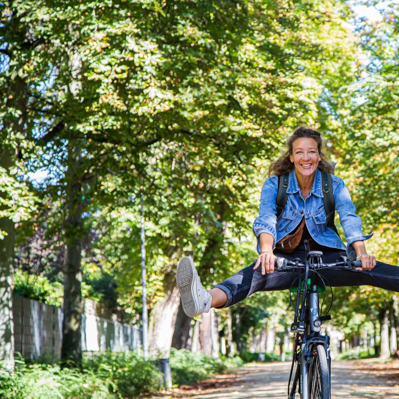 Foto: Eine Frau f&auml;hrt auf einem Fahrrad durch eine Allee und streckt die Beine in die Luft.