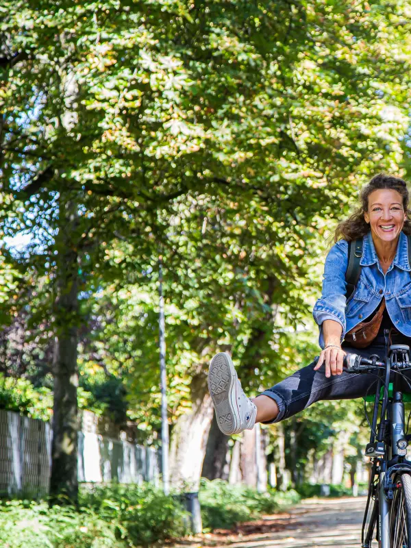 Foto: Eine Frau f&auml;hrt auf einem Fahrrad durch eine Allee und streckt die Beine in die Luft.