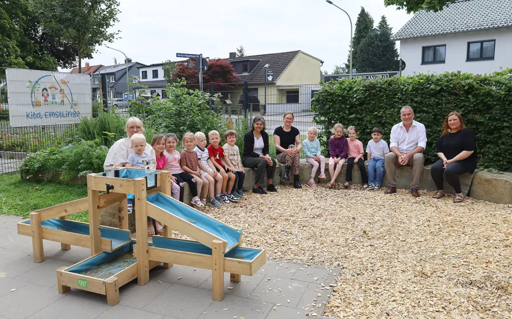 Foto: Neben dem Wasserspiel sitzen die Kinder mit den oben aufgez&auml;hlten Personen.