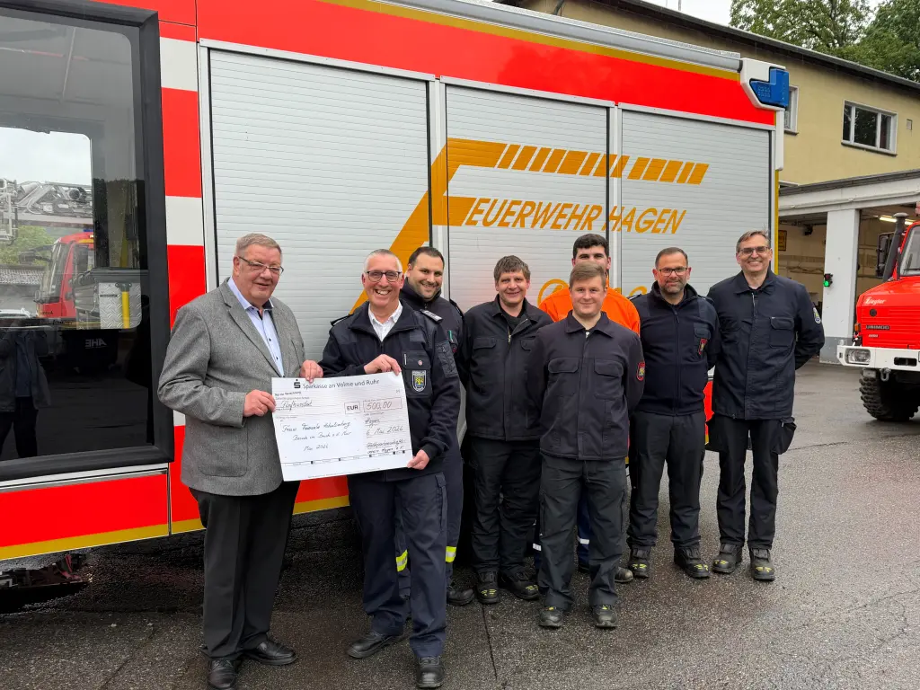 Foto: B&uuml;rgermeister Ralf Quardt &uuml;bergibt den Scheck von 500 Euro an Mitglieder der freiwilligen Feuerwehr. Im Hintergrund ist ein Feuerwehrauto zu sehen.