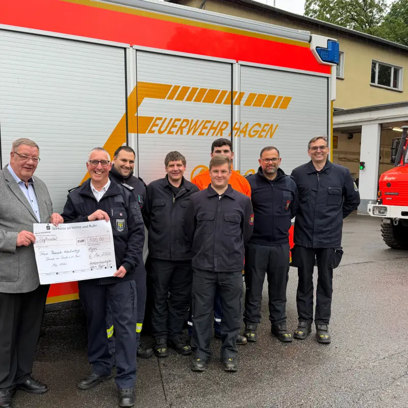 Foto: B&uuml;rgermeister Ralf Quardt &uuml;bergibt den Scheck von 500 Euro an Mitglieder der freiwilligen Feuerwehr. Im Hintergrund ist ein Feuerwehrauto zu sehen.