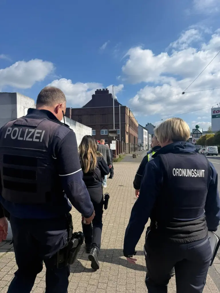 Foto: Mitarbeitende von polizei und Ordnungsamt laufen auf einem B&uuml;rgersteig auf eine H&auml;suerzeile zu.