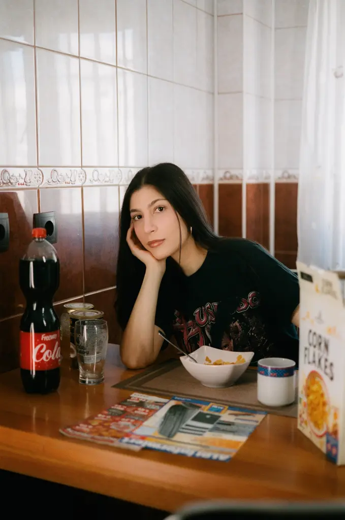 Foto: Eine Frau mit dunklen, langen Haaren sitzt an einem Esstisch. Neben ihr stehen eine Cornflakespackung sowie Colaflaschen, vor ihr steht eine Schlae mit Cornflakes und davor liegen Werbeprospekte.