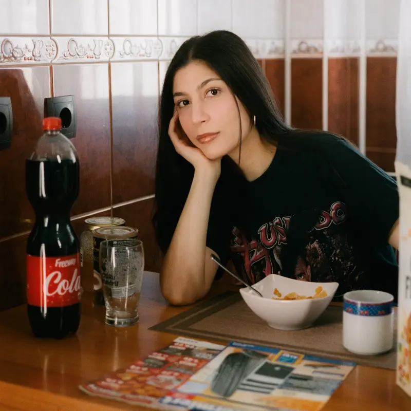 Foto: Eine Frau mit dunklen, langen Haaren sitzt an einem Esstisch. Neben ihr stehen eine Cornflakespackung sowie Colaflaschen, vor ihr steht eine Schlae mit Cornflakes und davor liegen Werbeprospekte.