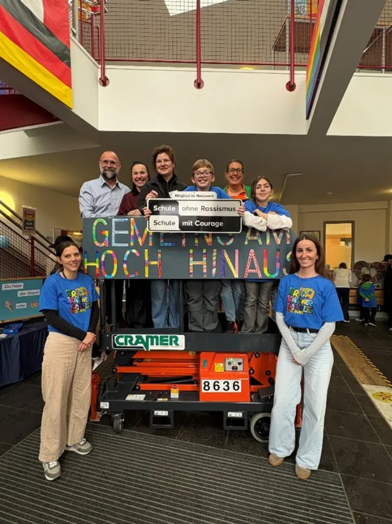 Foto: Mehrere Personen stehen auf einem Hubwagen und halten ein Schild "Gemeinsam hoch honaus" und "Schule ohne Rassismus - Schule mit Courage" hoch.