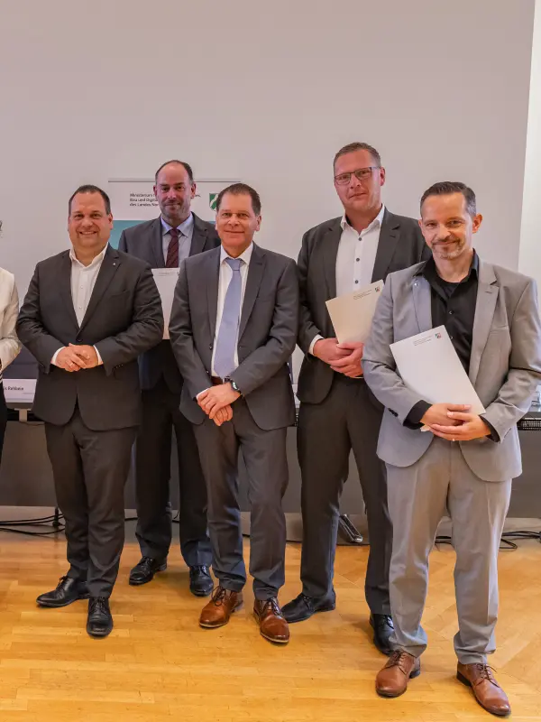 Foto: Die in der Bildzeile aufgef&uuml;hrten Personen stehen nebeneinander und halten den unterezichneten Vertrag in den H&auml;nden.